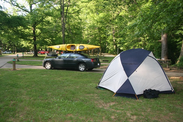 a tent in the campground with a car and kayak in the background
