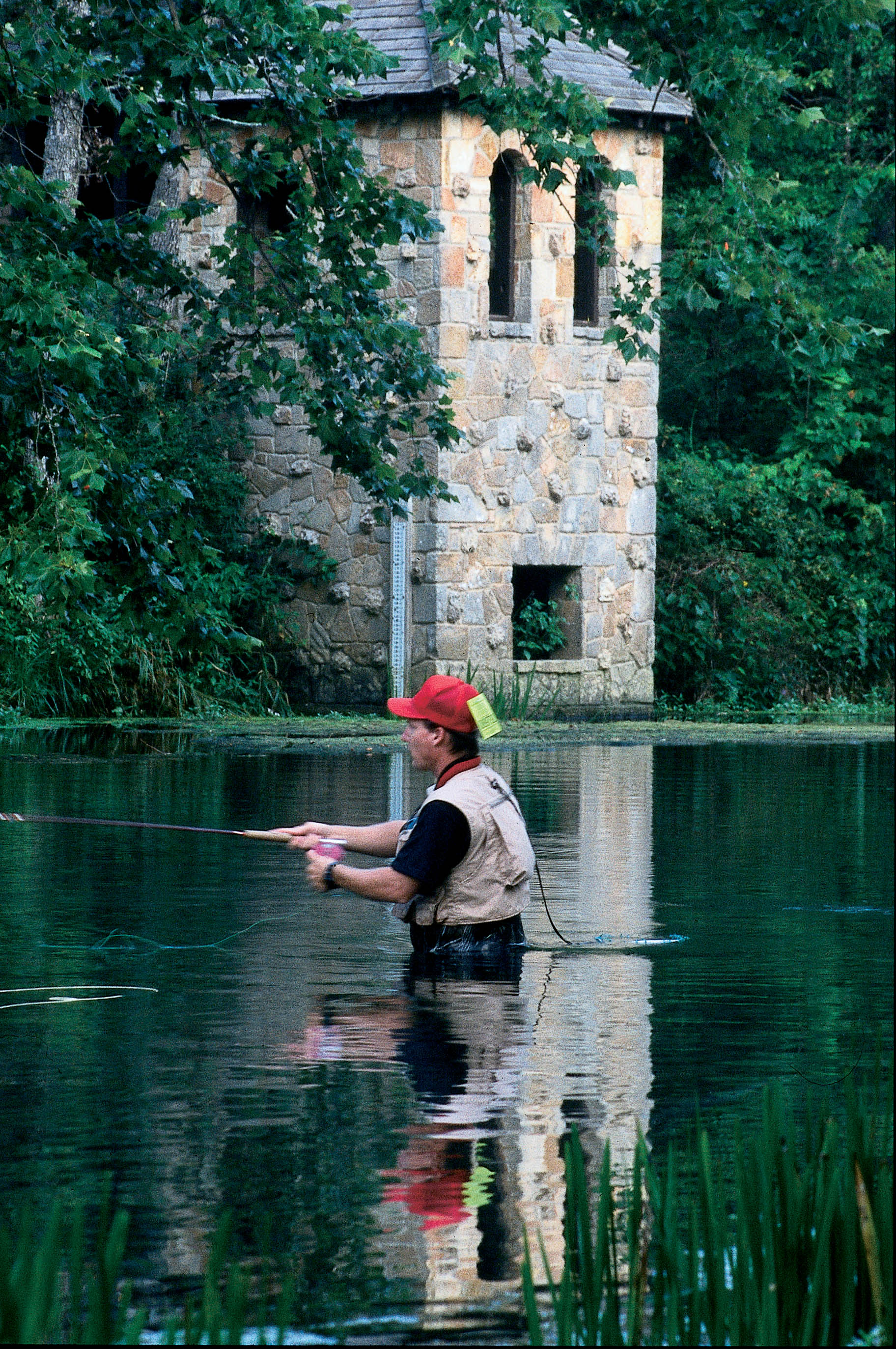 A man wading in the water fishing in front of one of the historic structures at Bennett Spring State Park