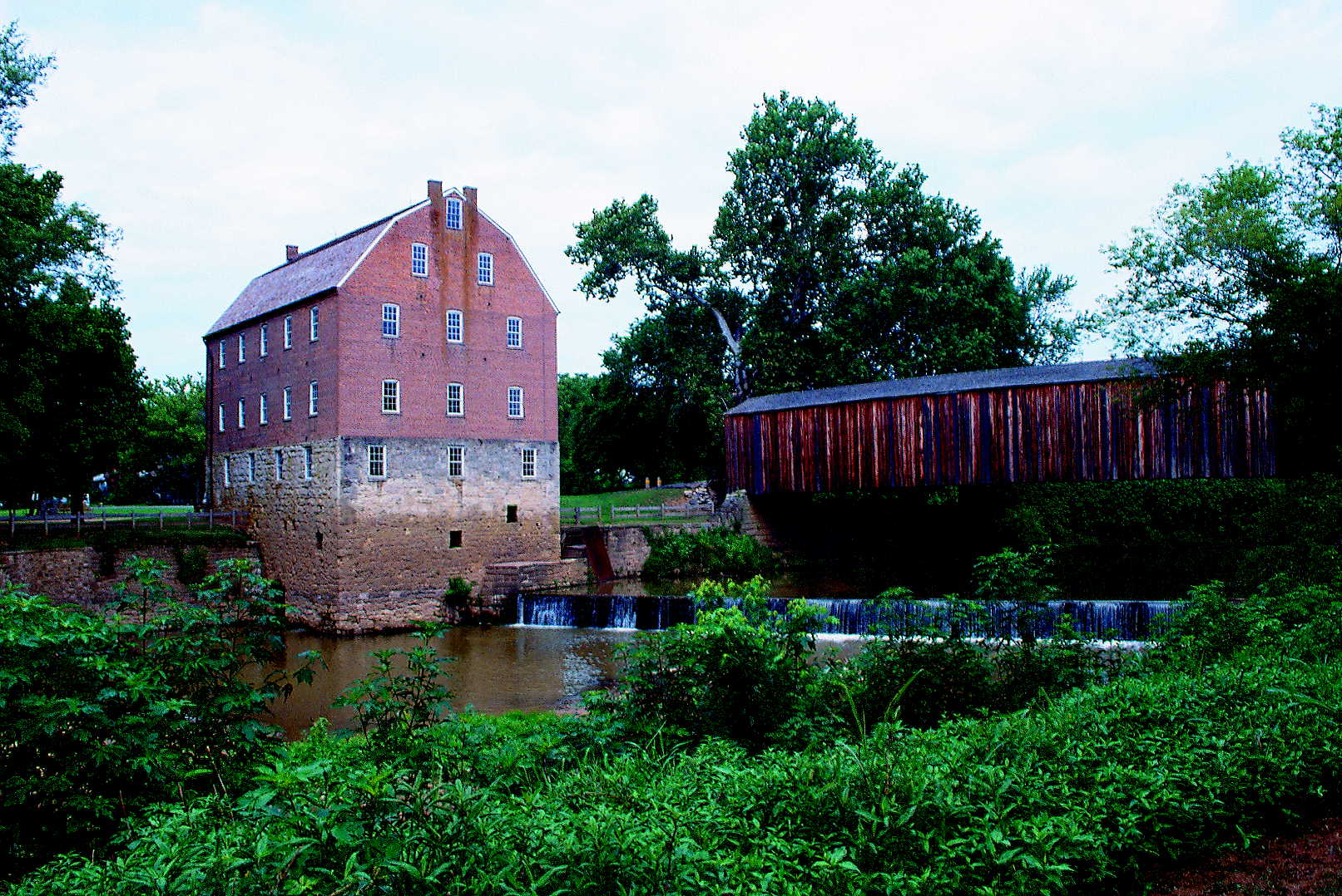 scenic view of the four-story red mill and adjacent covered bridg with water cascading below it