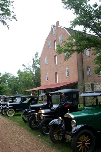 several vintage old cars parked in front of the mill