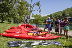 people taking a kayaking class standing on the shore listening to instruction