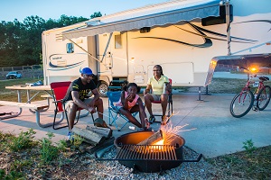 family sitting in front of camper around campfire