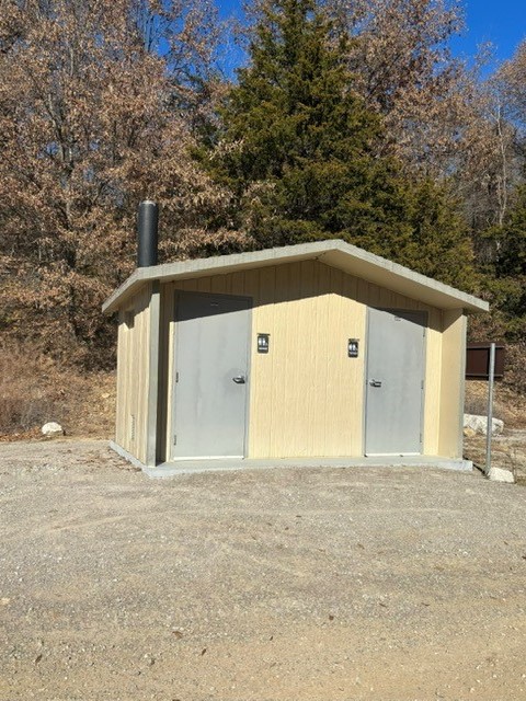 Small cream-colored building with gray doors and men's and women's restrooms signs