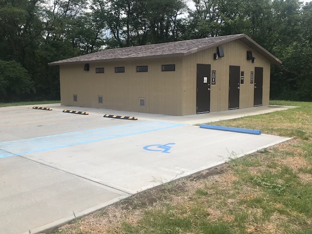 Exterior of showerhouse shows three showers and accessible parking spot