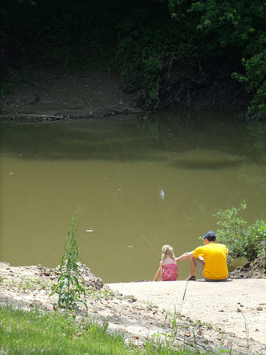 a father and daughter sit on the boat ramp and fish in the river