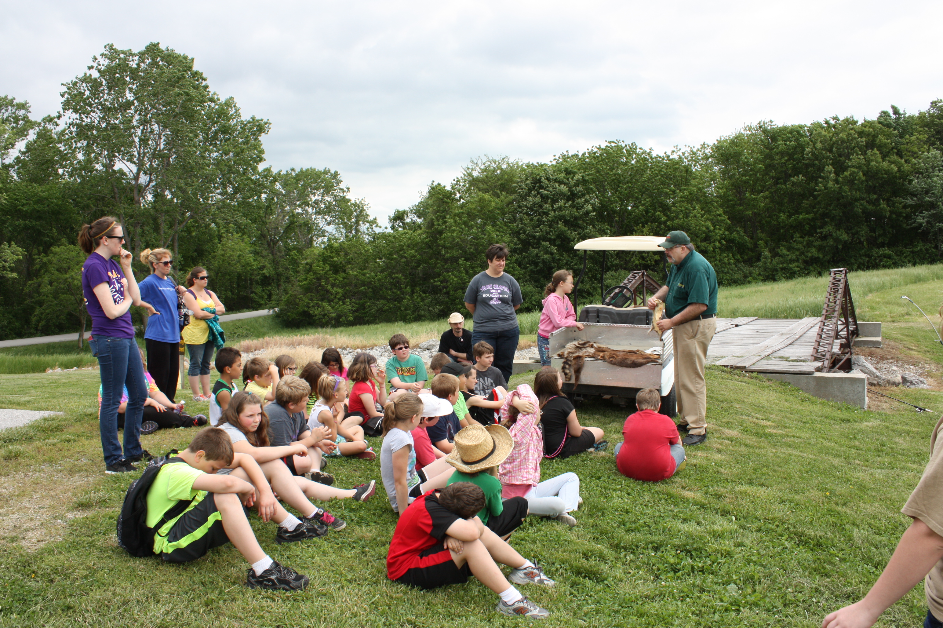 kids sit on the grass and listen to an interpreter