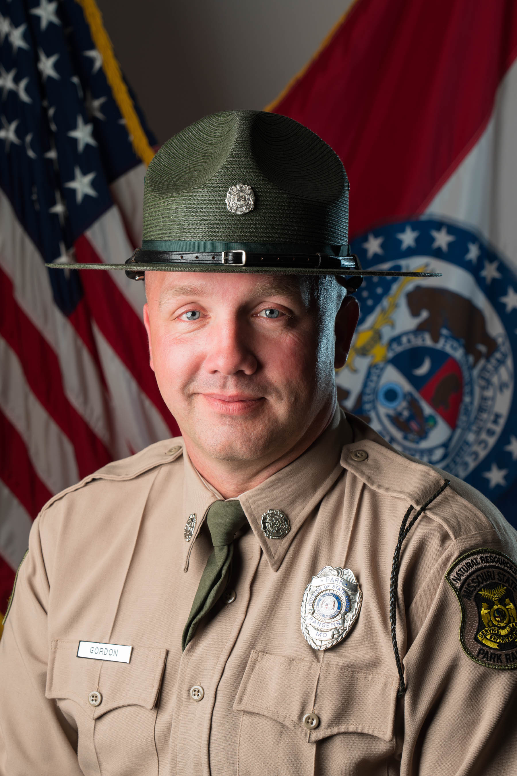 Sergeant Jason Gordon in hat and uniform with U.S. and Missouri flags in background