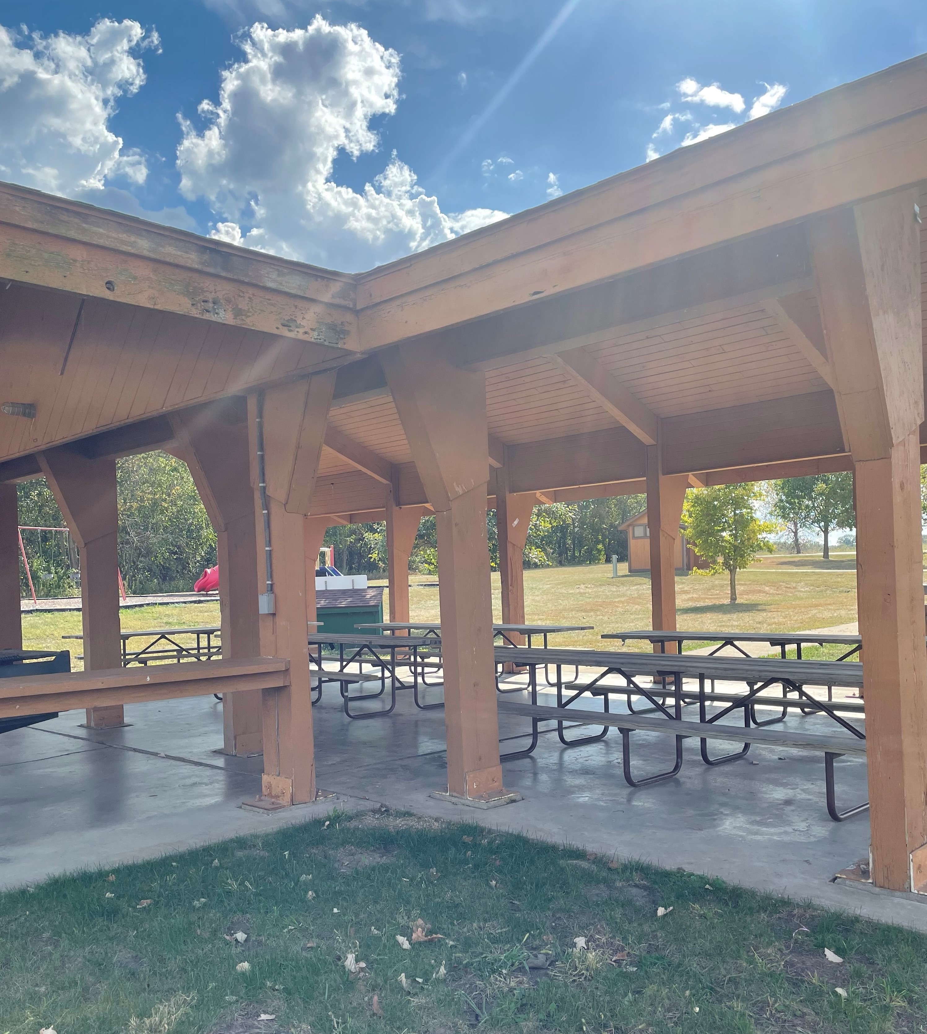 Picnic tables under the roof of the open shelter, with a playground in the background