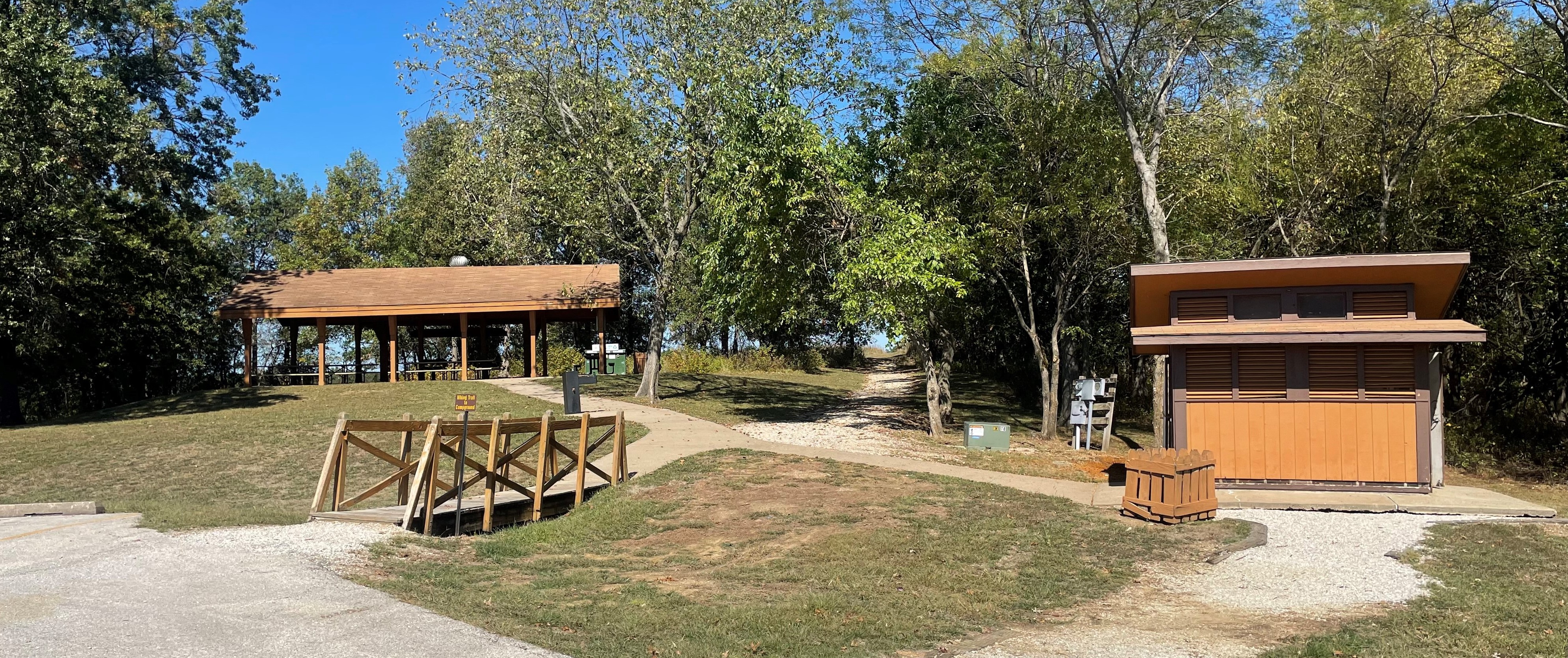 Open picnic shelter with footbridge and restroom in the foreground