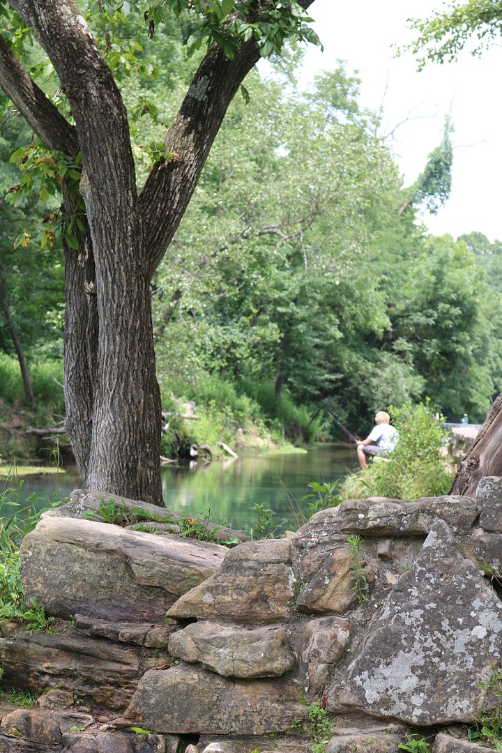 a man stis on the bank of the river fishing