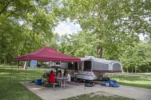 a family sitting under a shade tent at a picnic table next to their camper