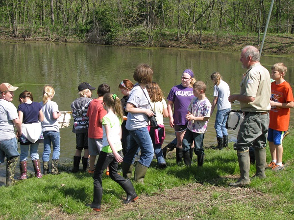 a group of kids listening to a nature program by the lake