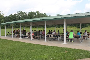 a large group is gathered for a program under one of the park's picnic shelters