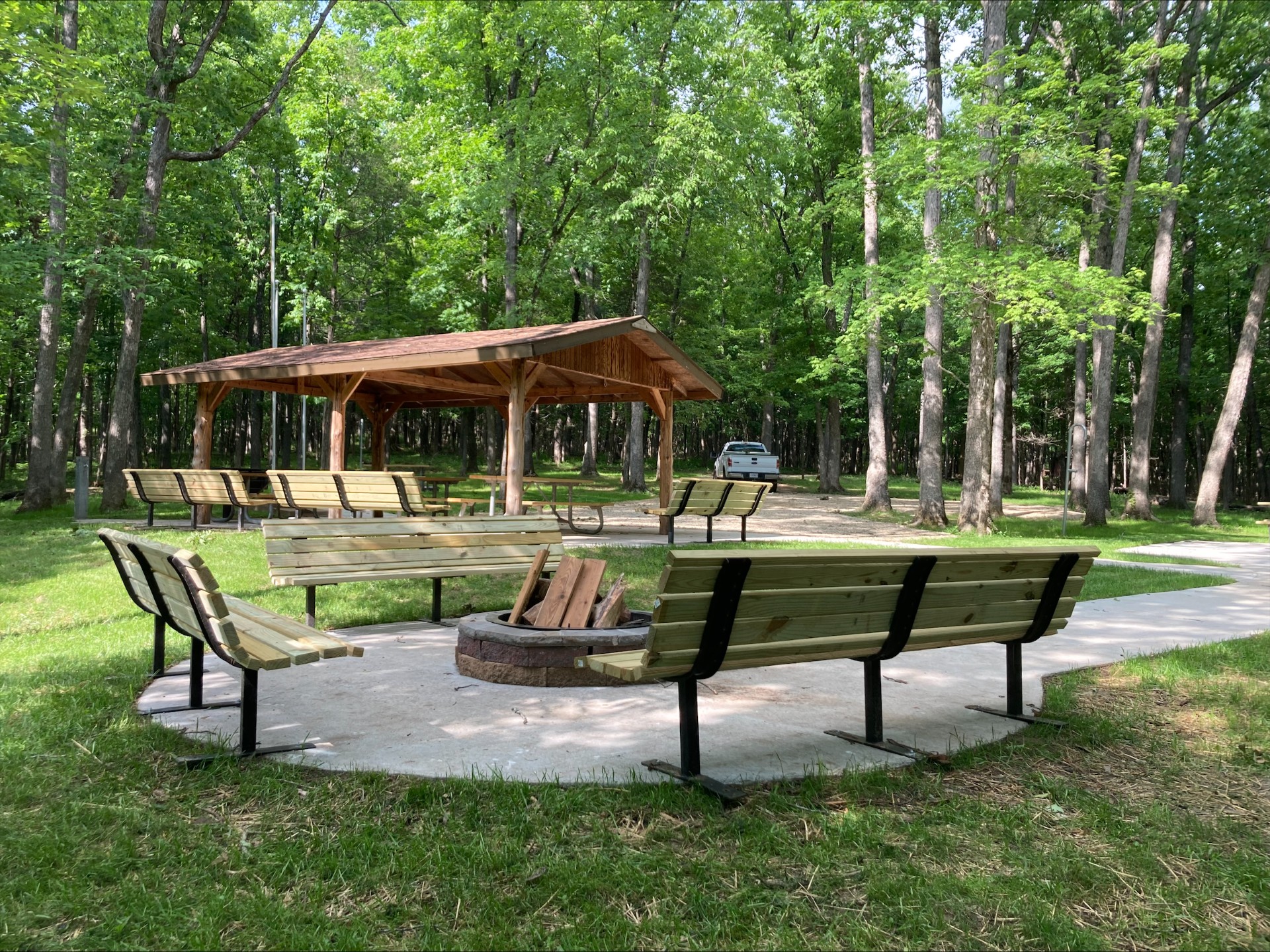 Group campfire pit surrounding by benches, with covered meeting area in background