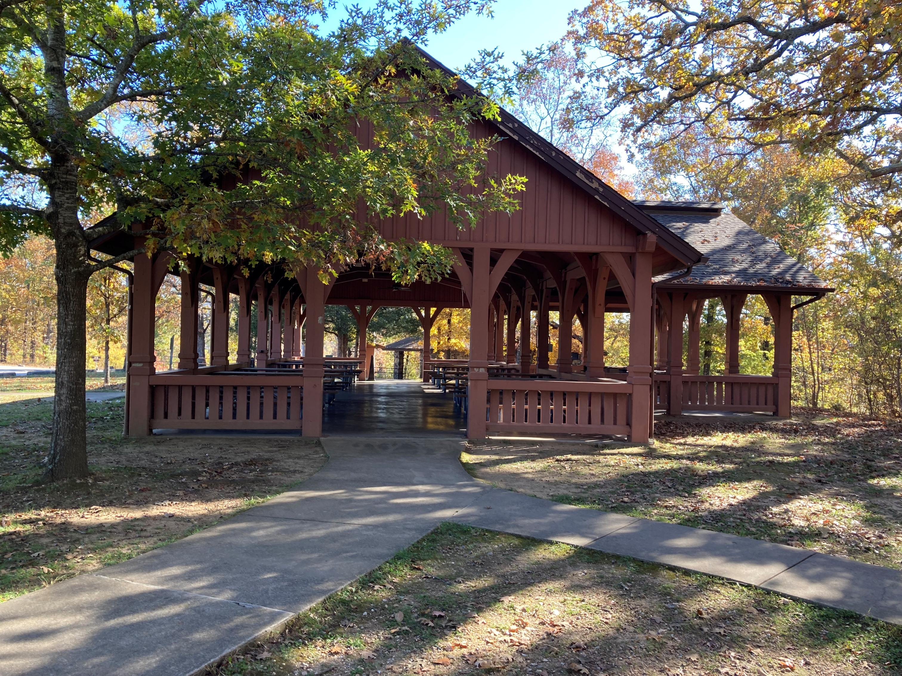 Two sidewalks converge and lead up to the open shelter, which is surrounded by trees with green and yellow leaves