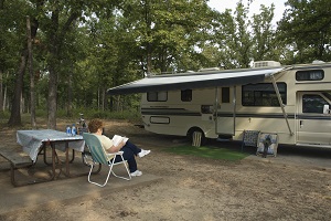 a woman sitting in a lawn chair reading a book outside of her camper