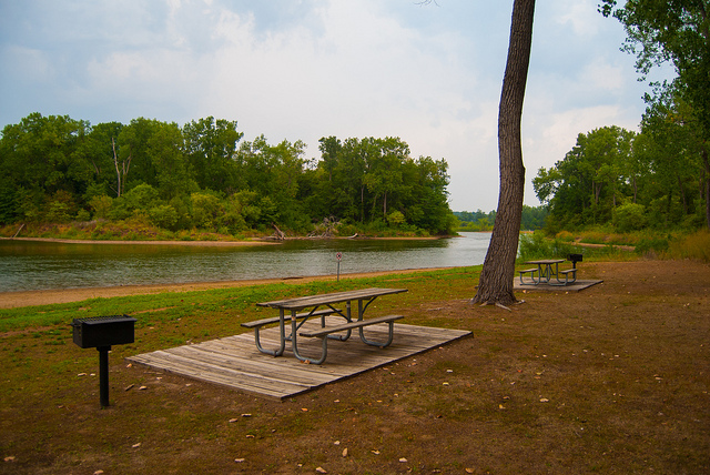 a picnic table on a wood platform and a grill close to one of the lakes