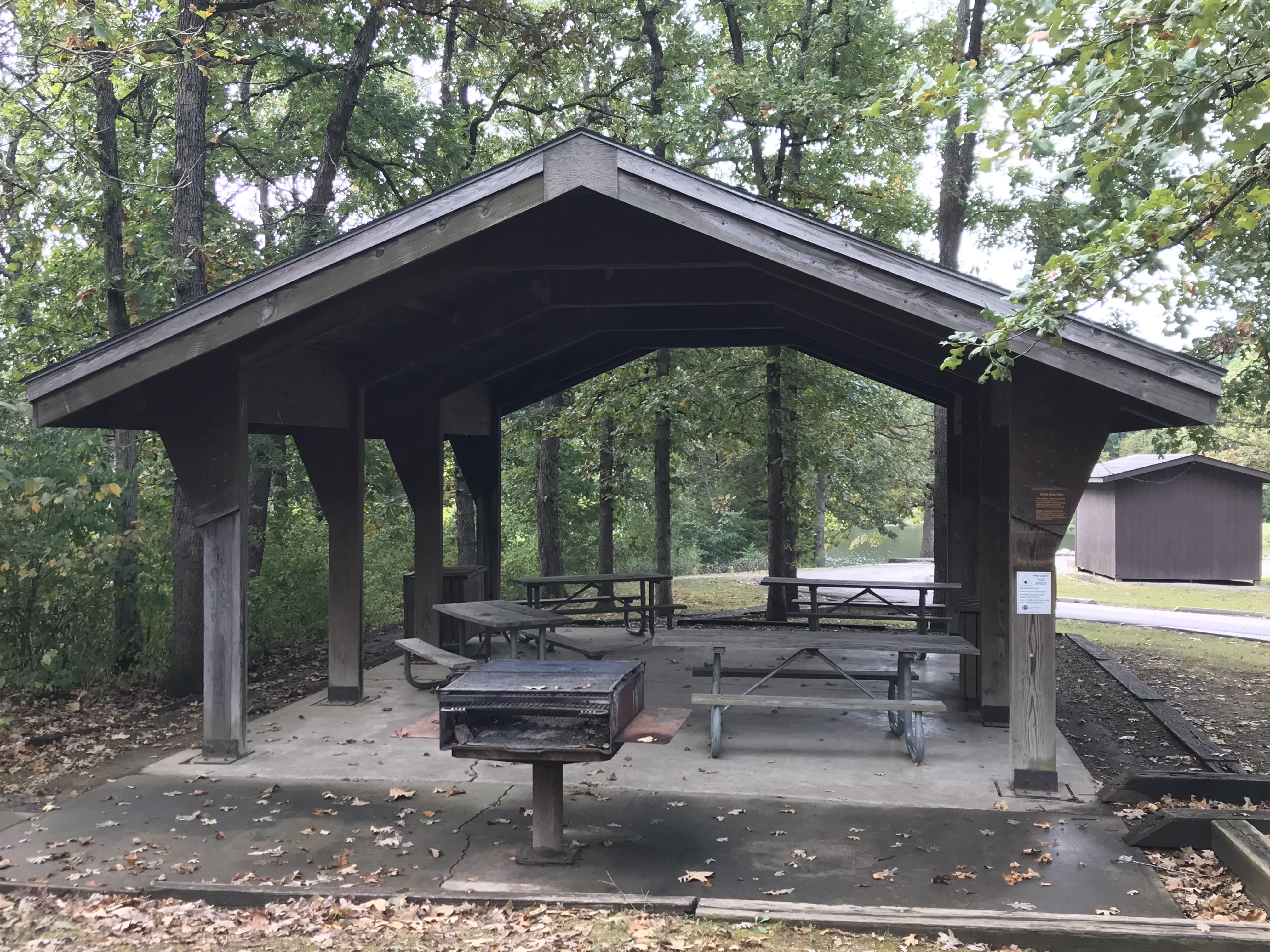 Open picnic shelter with picnic tables, a grill and a trash receptacle