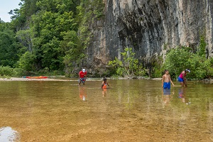 people swimming in the creek next to the bluff