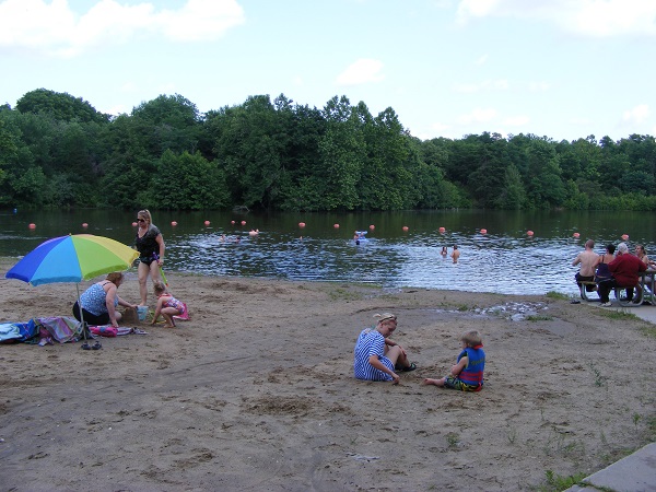 people sitting on the sand beach and swimming in the lake