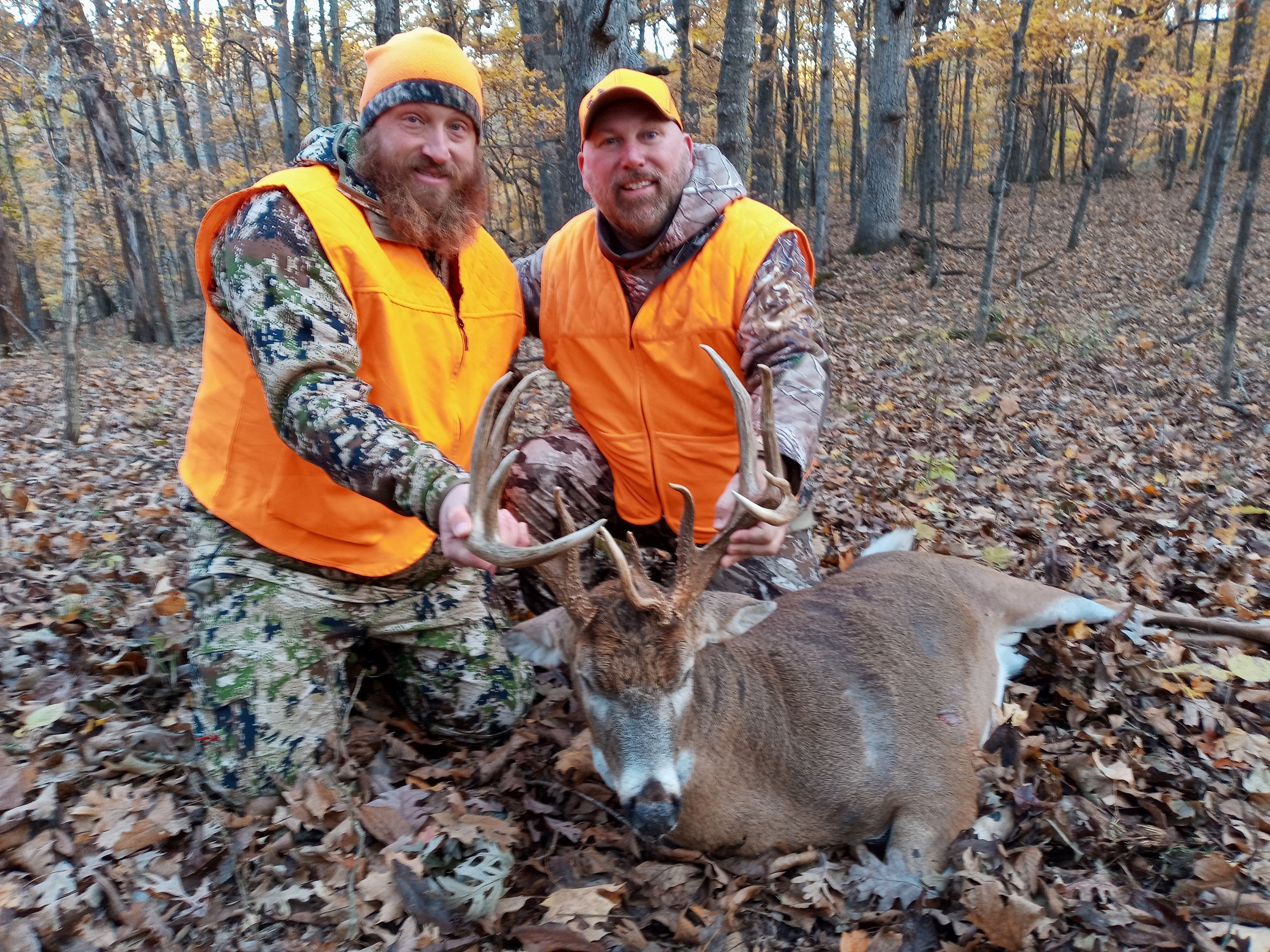 A veteran and a guide in camoflauge and hunter orange pose in the woods with a large buck, the recipient of the Biggest Buck Award for 2021.