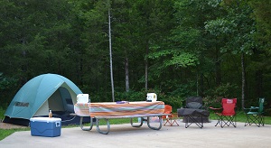 tent , a cooler and lawn chairs set up next to a picnic table on a campsite