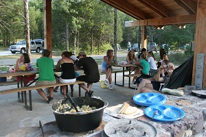 large group enjoying dinner under one of the campground picnic sheltes