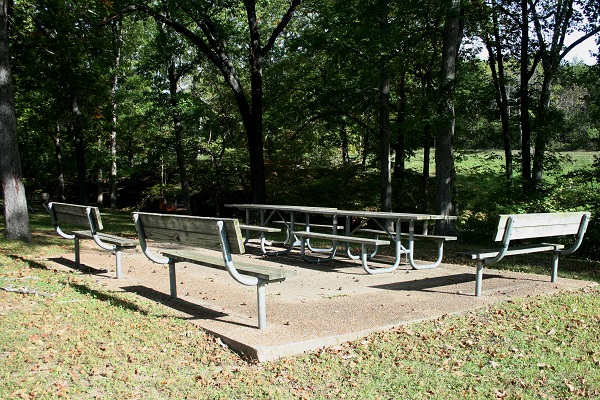 group picnic area with two tables and three separate benches on a concrete pad