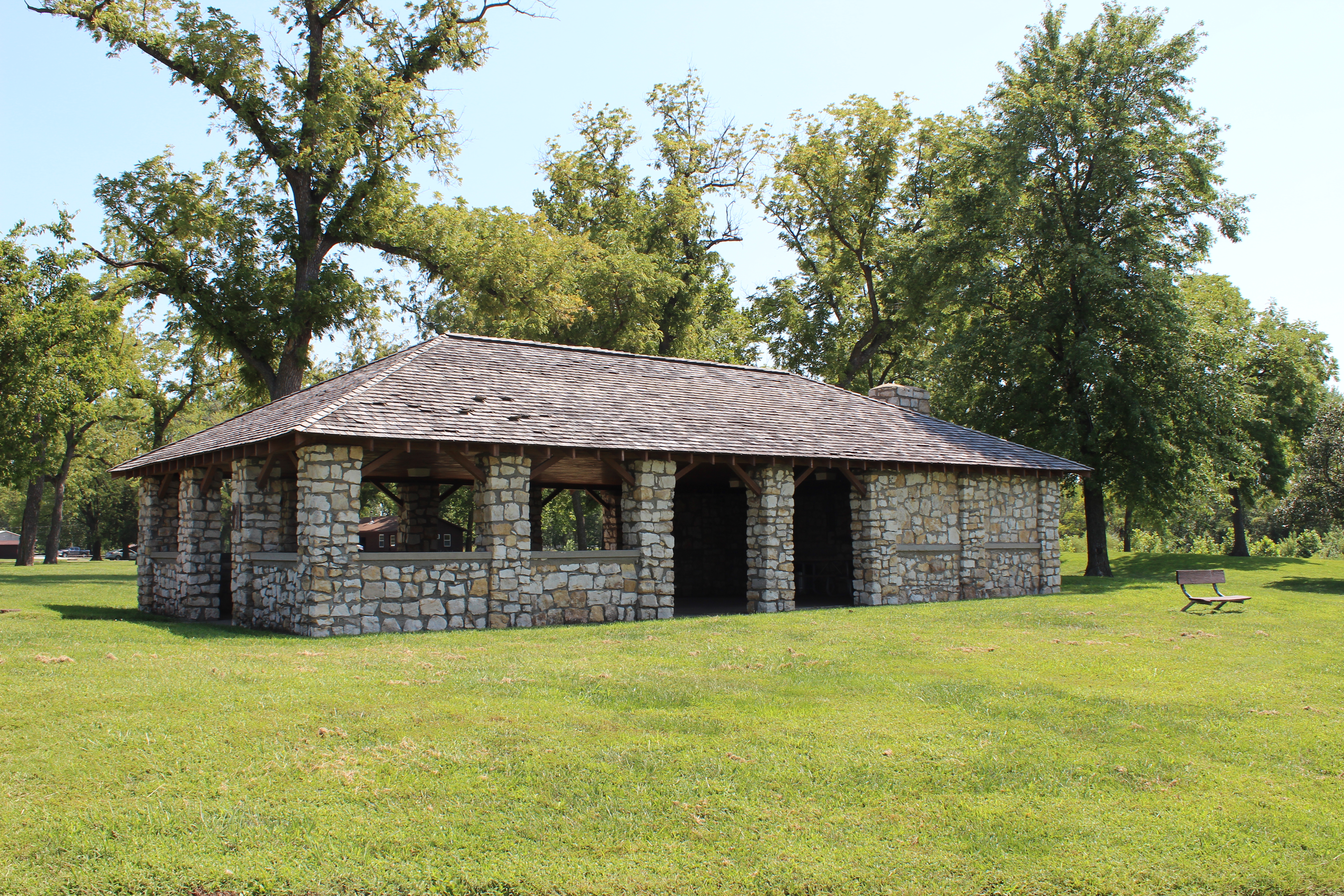 Stone picnic shelter with open windows and doorways situated in field under trees