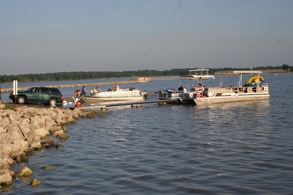 a boat unloading on the boat ramp while a pontoon boat is pulled up to the dock