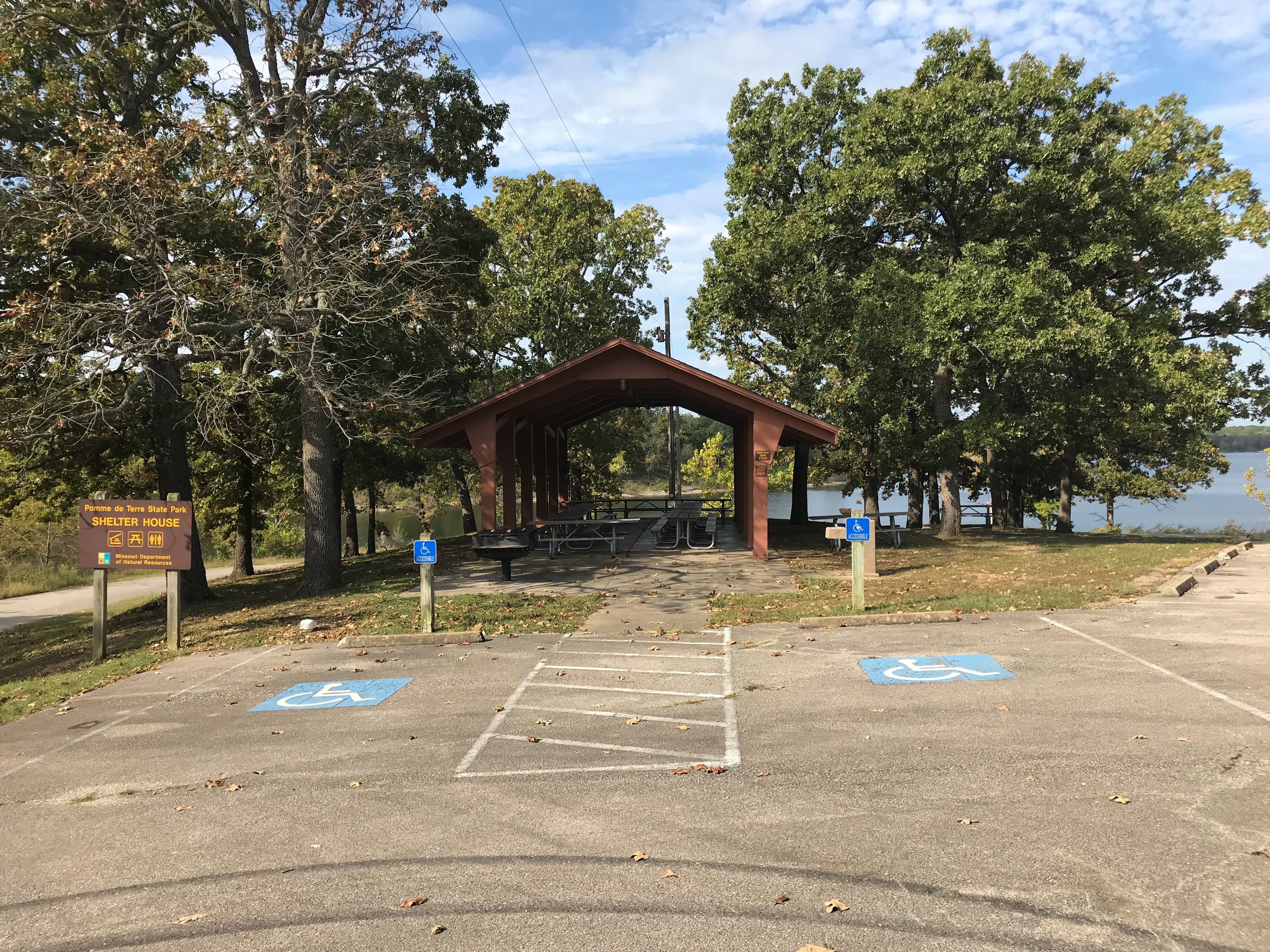 Open picnic shelter in front of lake with accessible parking spaces and shelter sign in foreground