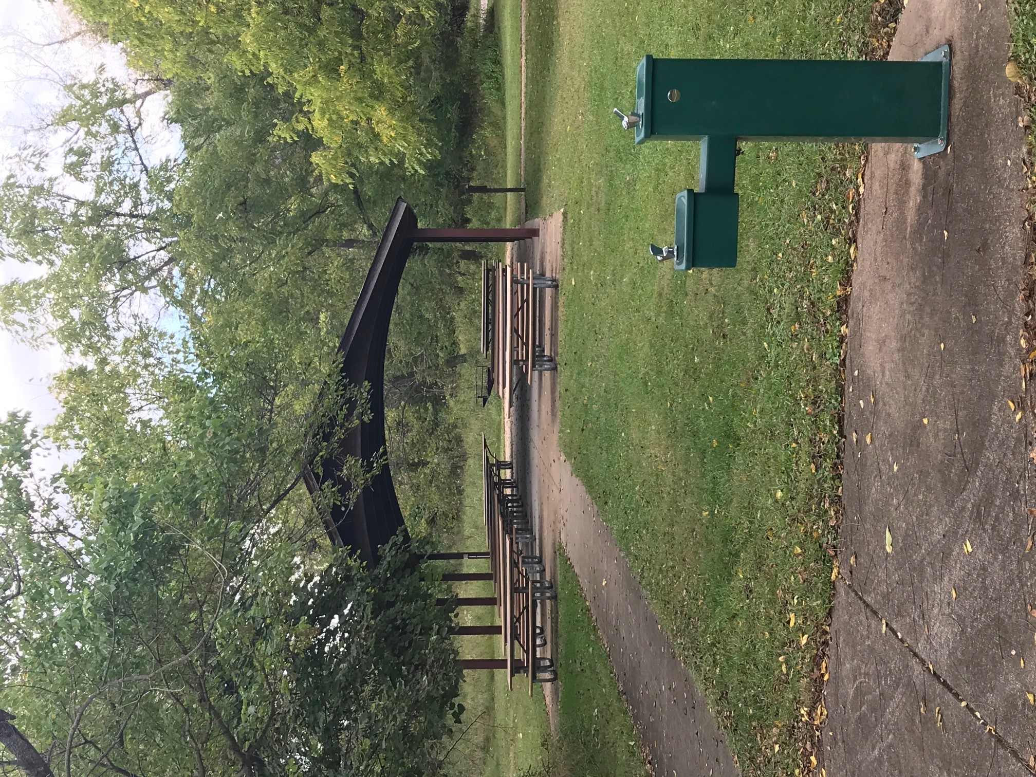 A water fountain stands on the sidewalk that leads to the open picnic shelter