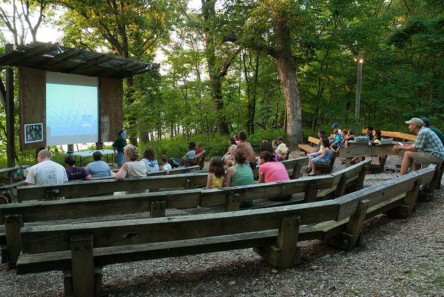 people sitting on the wooden benches of the amphitheater listening to a program