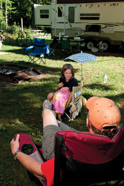 a man and little girl sitting in lawn chairs outside their camper