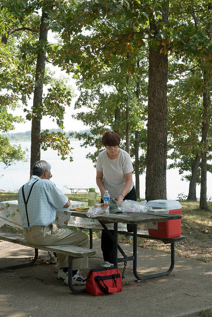 a couple enjoys lunch at a picnic table close to the lake