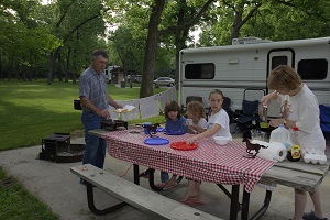 a family preparing to eat on the picnic table outside their camper