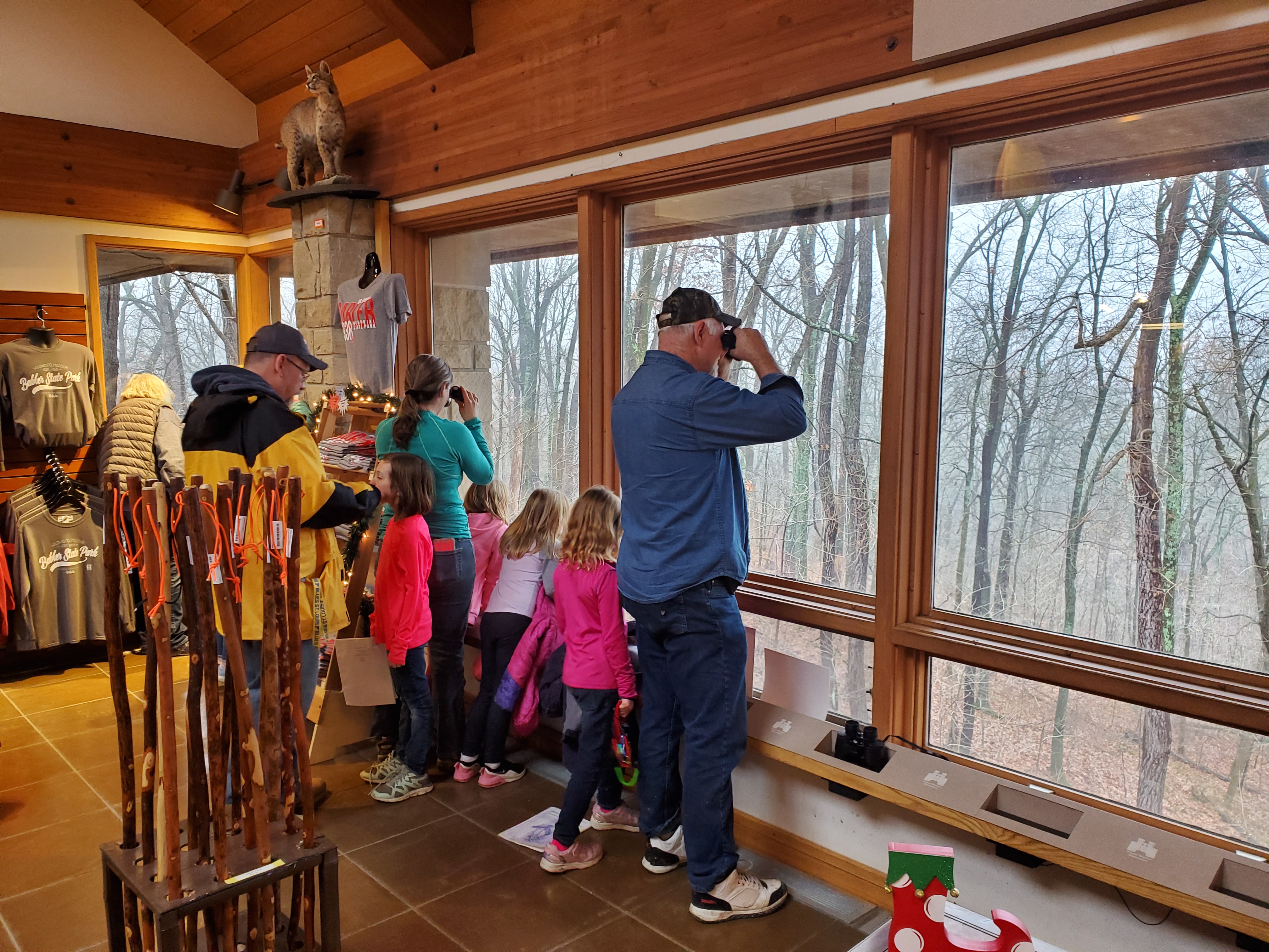 Guests at the visitor center's viewing area use binoculars to look into the woods through large windows