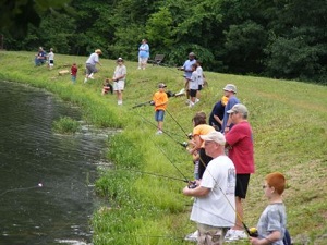 Several people and kids fishing in the lake from the shore