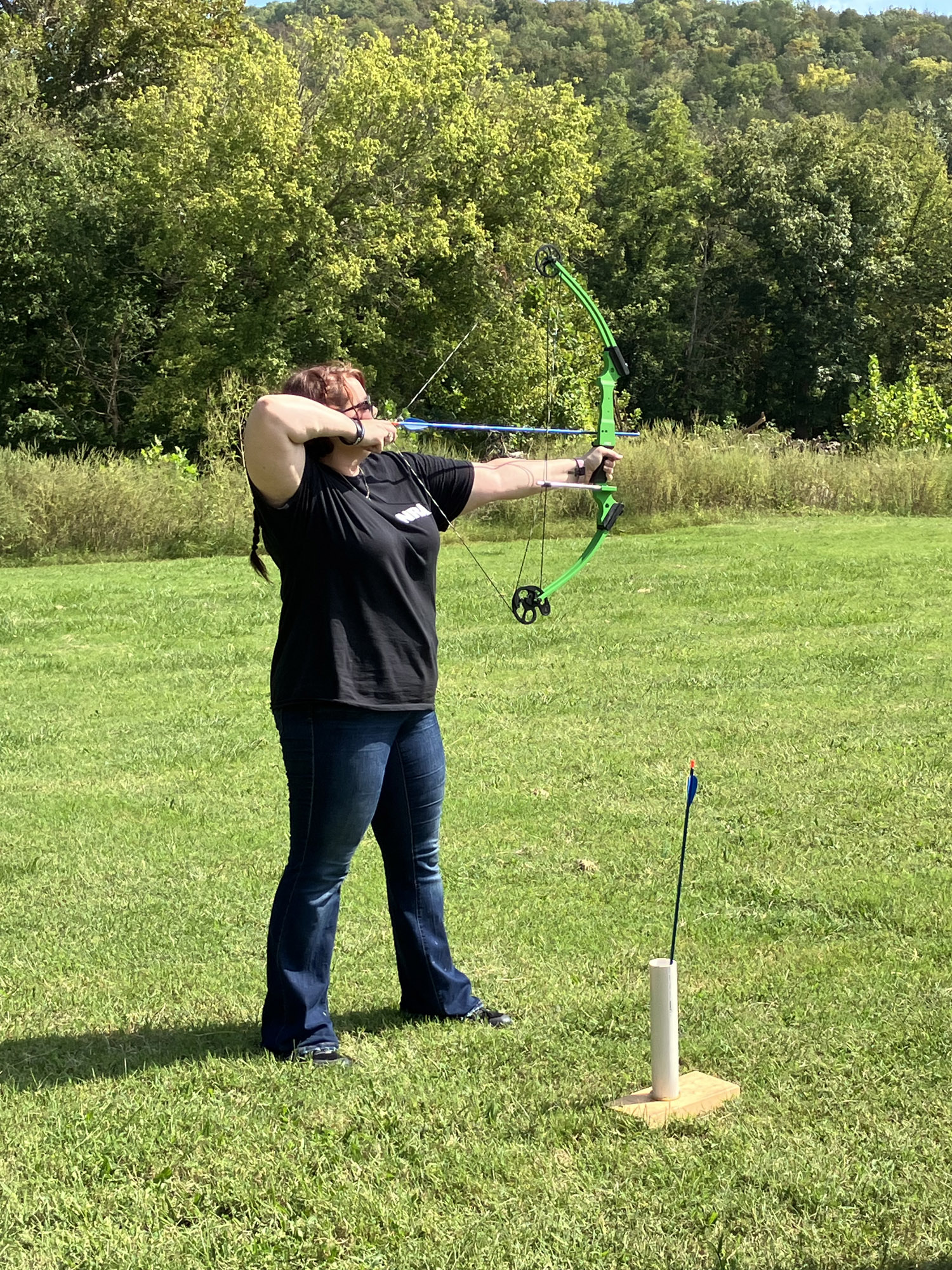 A woman standing in a field preparing to shoot an arrow from a bow